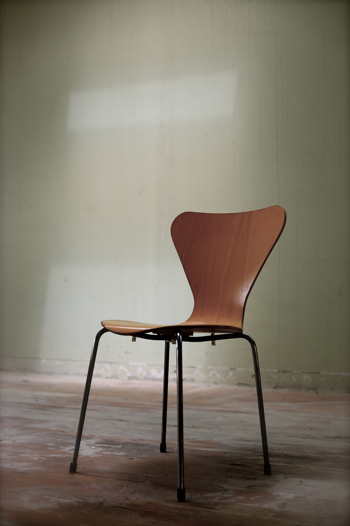 Artarene Simple wooden chair against a light green wall in an empty indoor room.