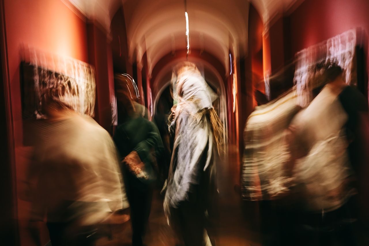 Artarene Abstract motion blur of people walking in a dimly lit art gallery hallway.